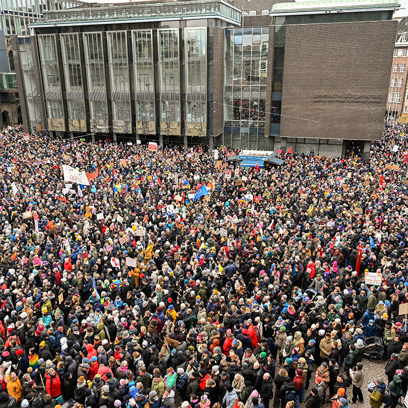 Eine große, bunt gemischte Menschenmenge bei einer Demonstration im Regenwetter zwischen Dom, Rathaus und Bürgerschaft.
